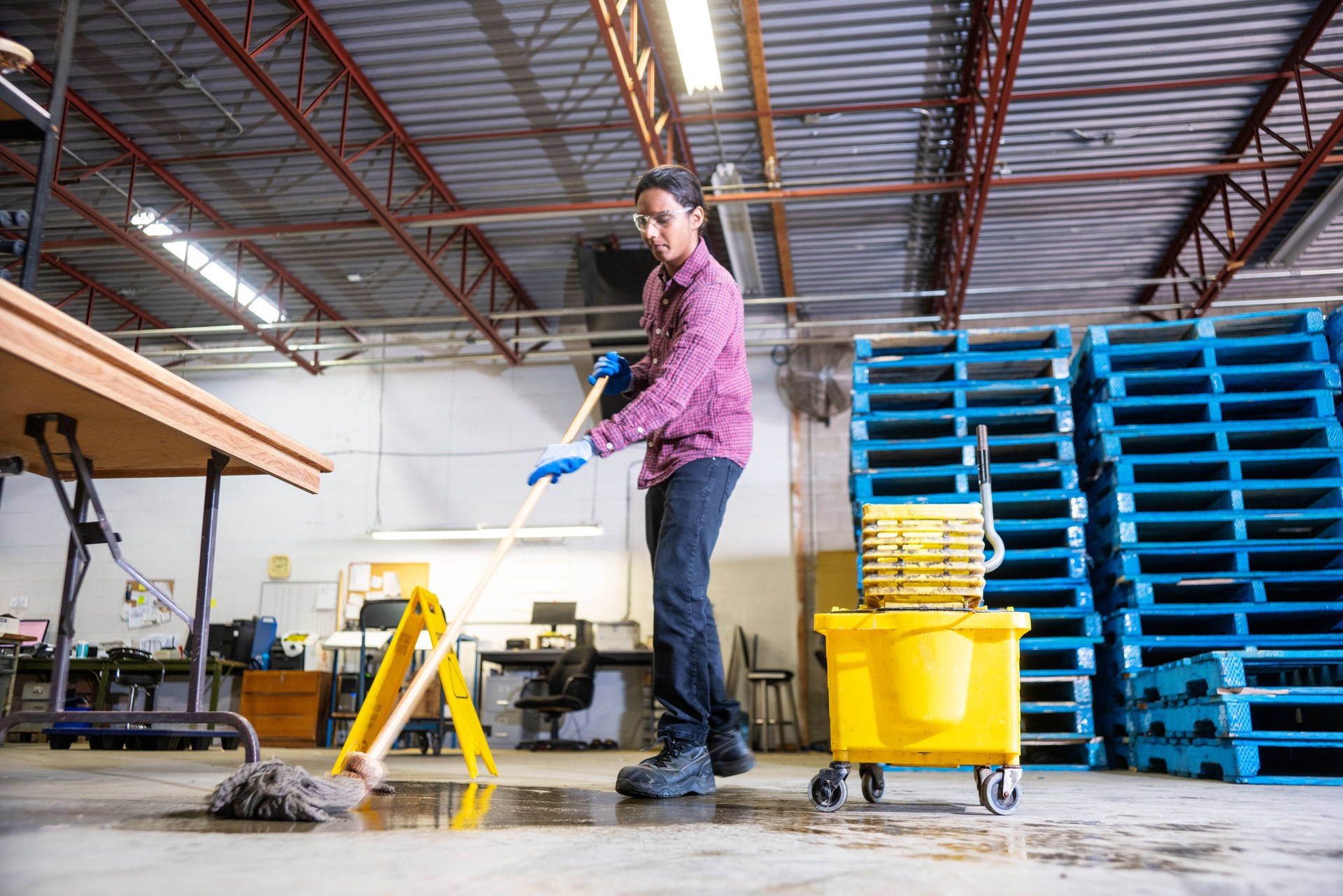 A worker in a warehouse cleaning-up a hazard of spilled liquid.